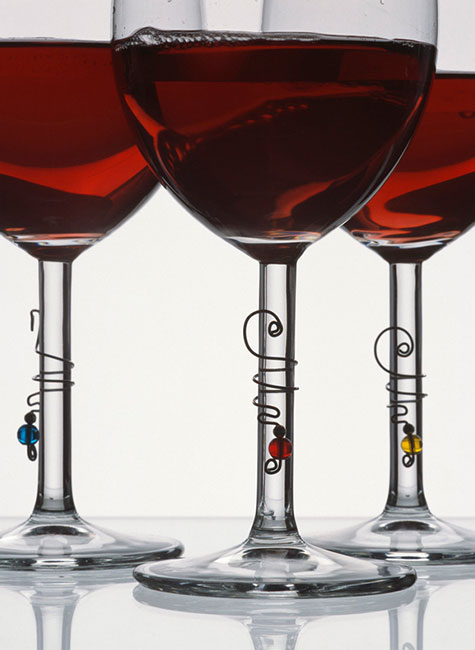 Three long stem wine glasses filled with red win with wine curls wrapped around the stems of the glass. Each wine curl with a different coloured bead. One yellow, one blue, one red. | Ear Curls, Ear Climbers
